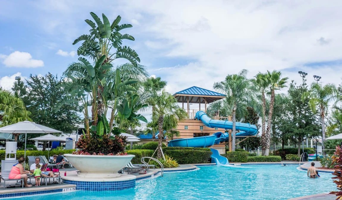Tropical resort swimming pool with a blue water slide and palm trees.