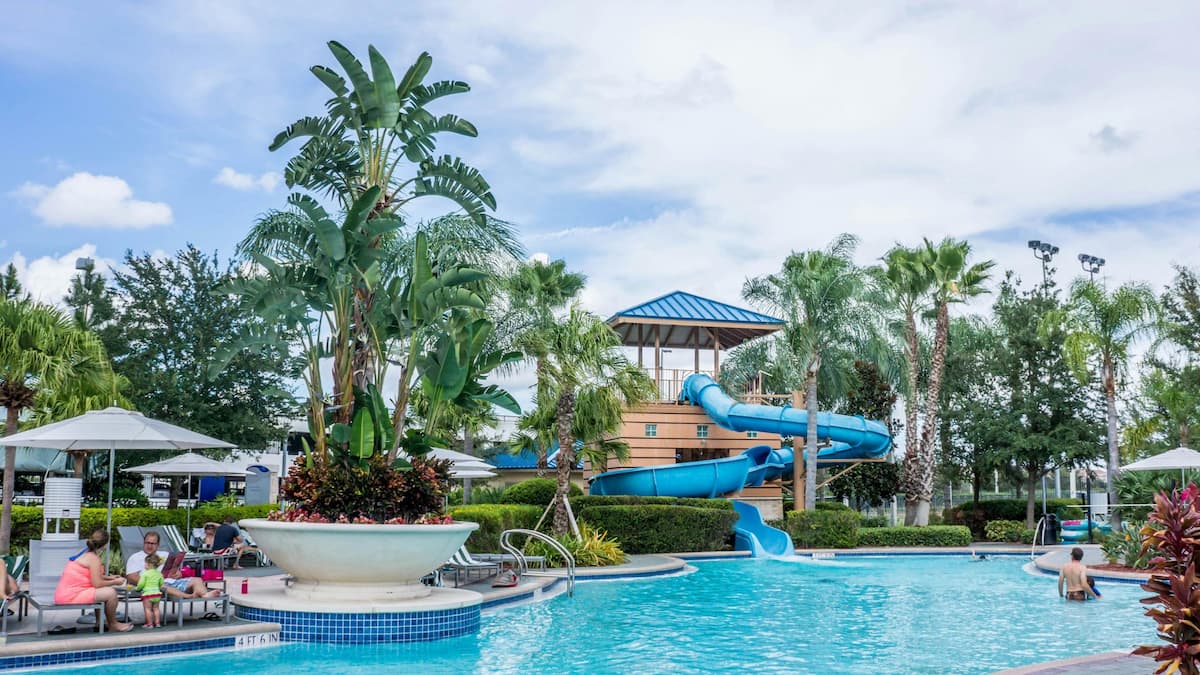 Tropical resort swimming pool with a blue water slide and palm trees.